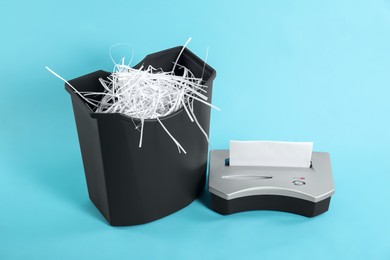 Photo of Shredder, basket and paper strips on light blue background