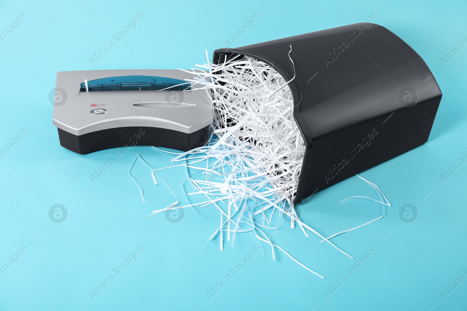 Photo of Shredder, basket and paper strips on light blue background