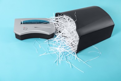 Shredder, basket and paper strips on light blue background