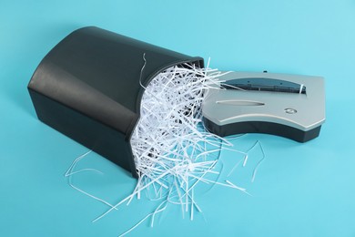 Photo of Shredder, basket and paper strips on light blue background