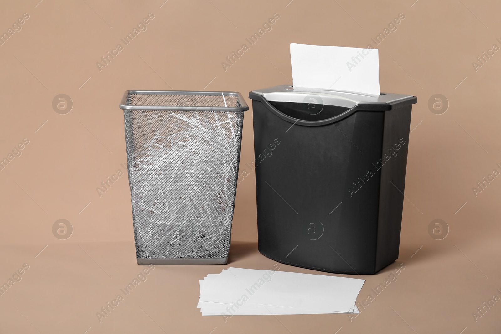 Photo of Shredder, metal basket and paper strips on beige background