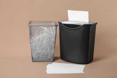 Photo of Shredder, metal basket and paper strips on beige background