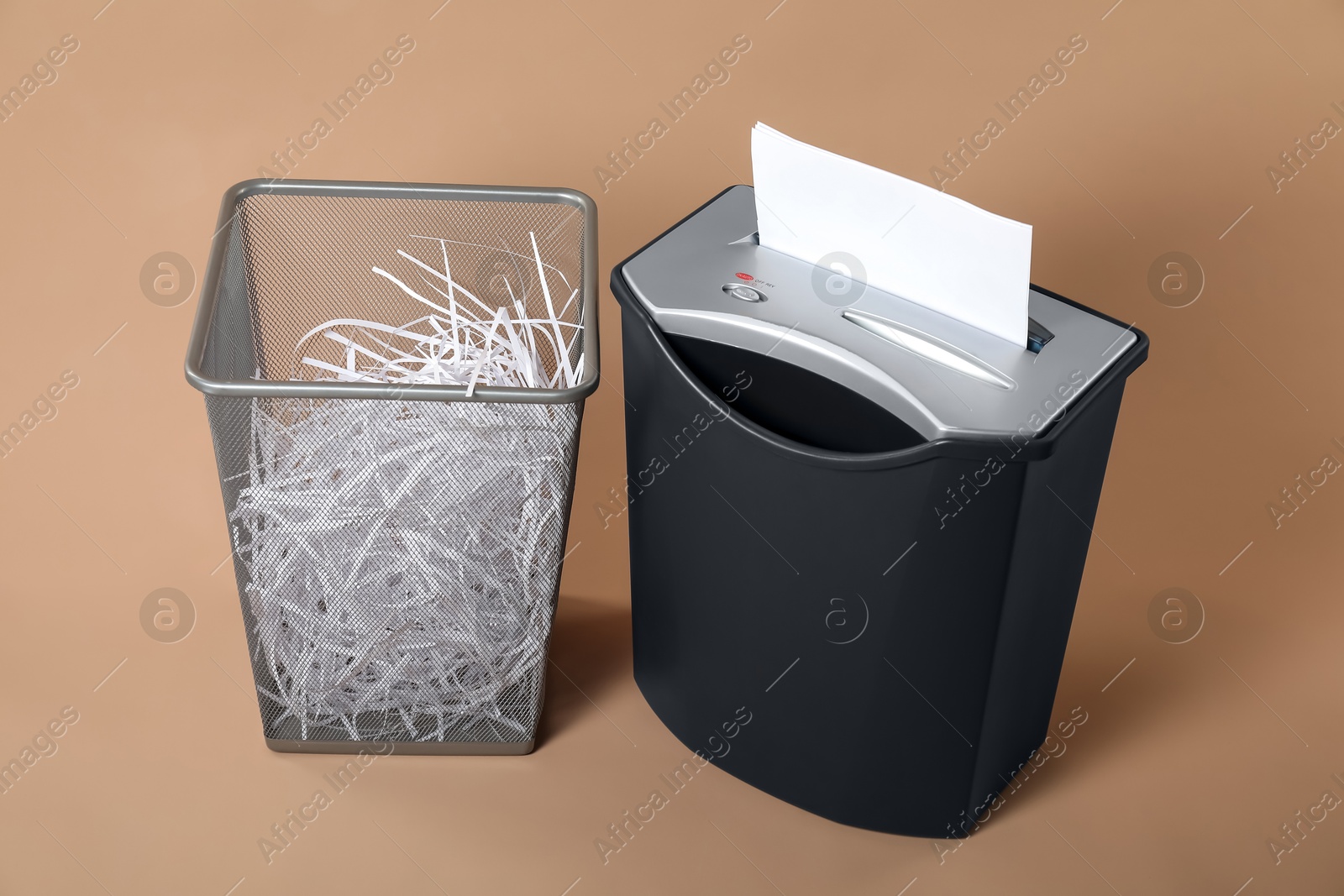 Photo of Shredder, metal basket and paper strips on beige background