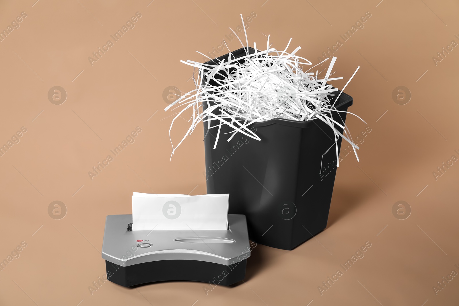 Photo of Shredder, basket and paper strips on beige background