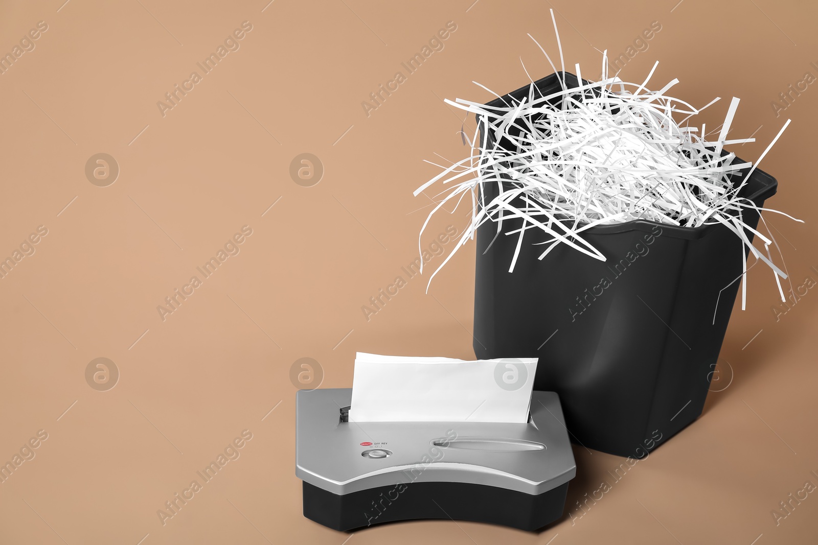 Photo of Shredder, basket and paper strips on beige background, space for text