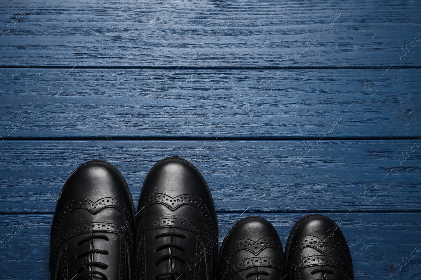 Photo of Big and small shoes on blue wooden table, top view. Space for text