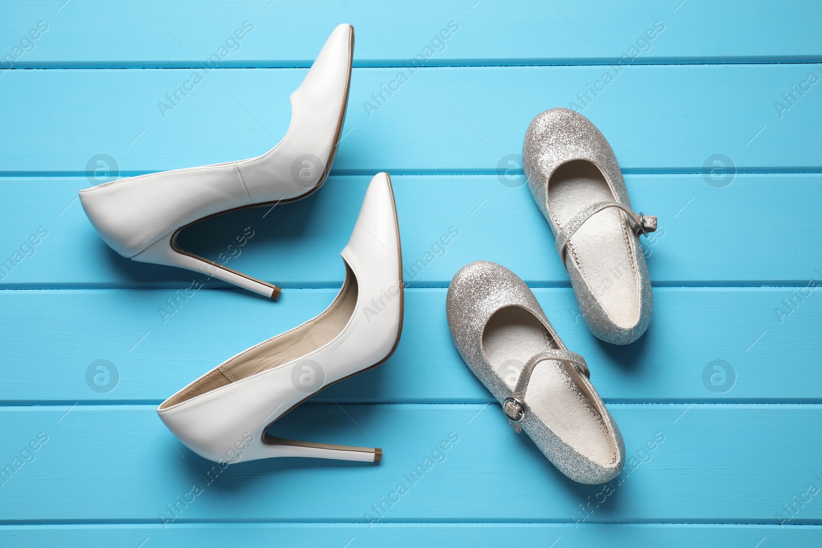 Photo of Big and small shoes on light blue wooden table, flat lay