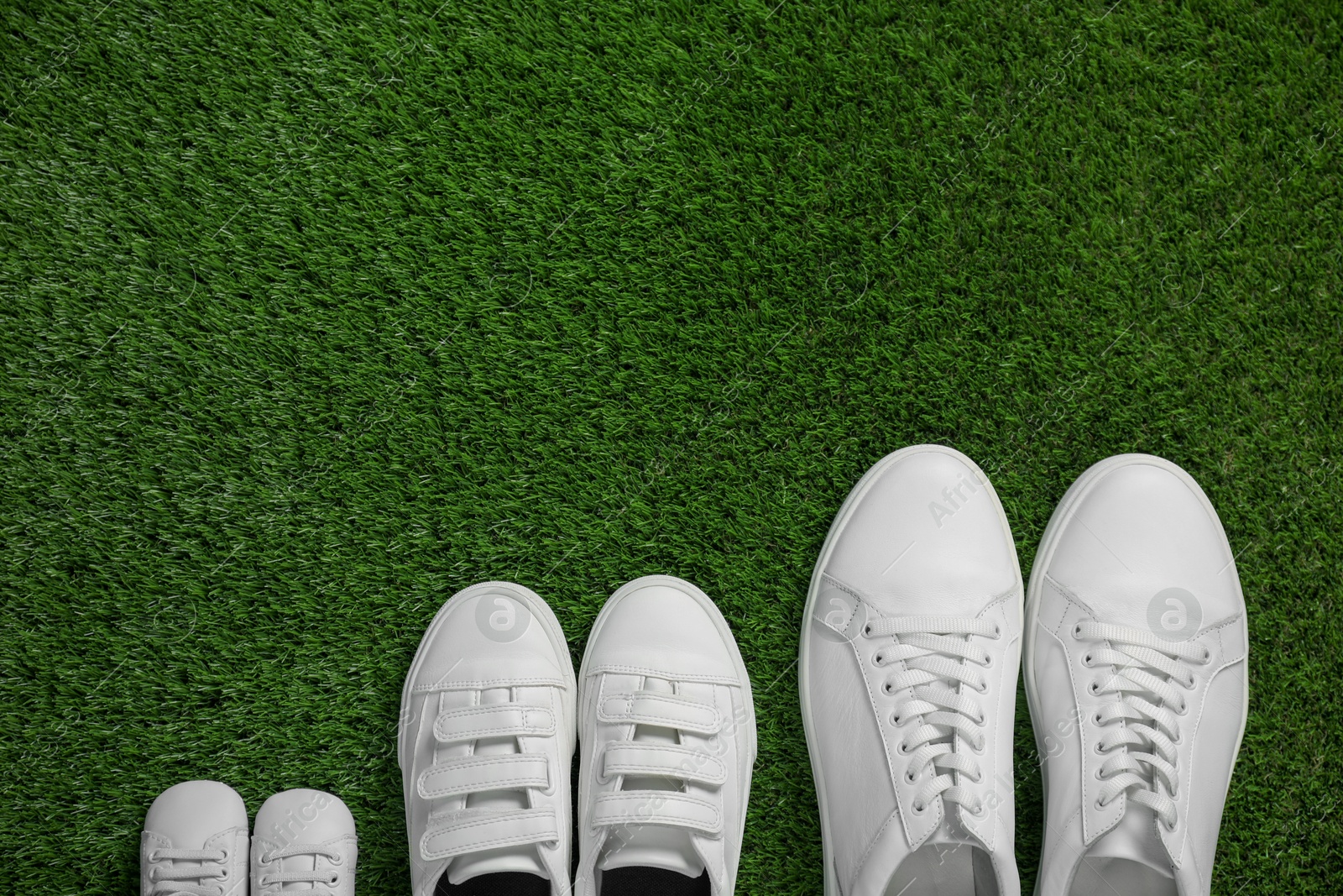 Photo of Big and small shoes on green grass, top view. Space for text