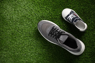 Photo of Big and small shoes on green grass, top view. Space for text