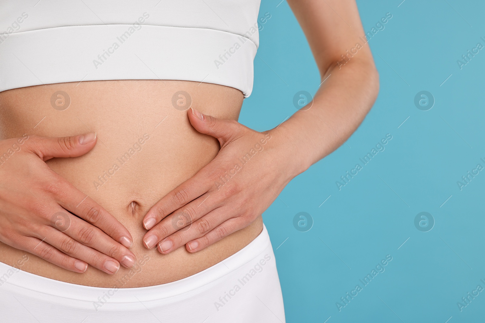 Photo of Healthy digestion. Woman touching her belly on light blue background, closeup