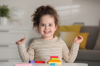 Portrait of smiling girl playing with wooden geometric figures at table indoors. Adorable child