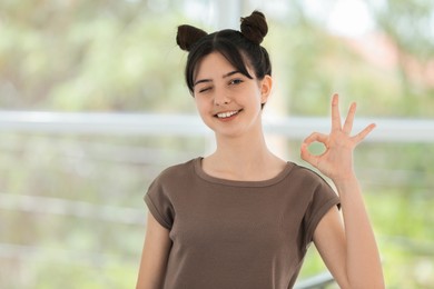 Portrait of smiling teenage girl showing ok gesture on blurred background