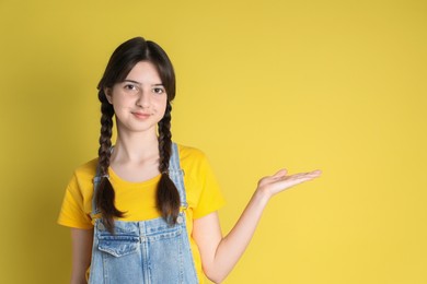 Photo of Portrait of cute teenage girl holding something on yellow background. Space for text