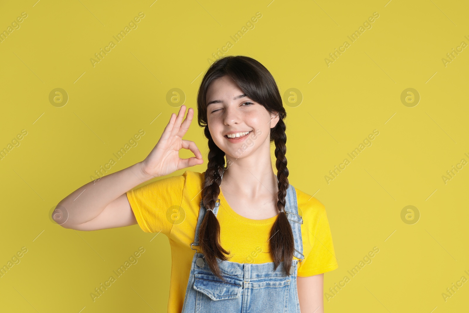 Photo of Portrait of smiling teenage girl showing ok gesture on yellow background