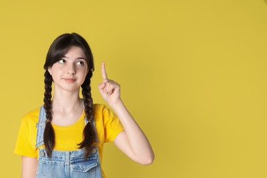 Photo of Portrait of cute teenage girl pointing at something on yellow background. Space for text