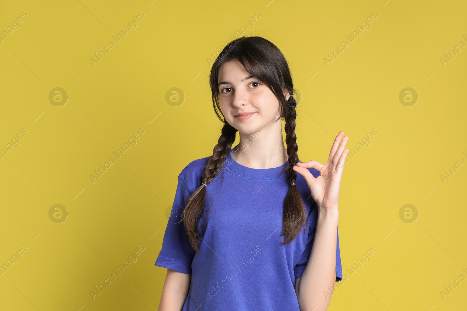 Photo of Portrait of cute teenage girl showing ok gesture on yellow background