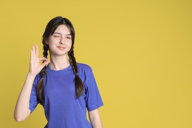 Portrait of cute teenage girl showing ok gesture on yellow background. Space for text