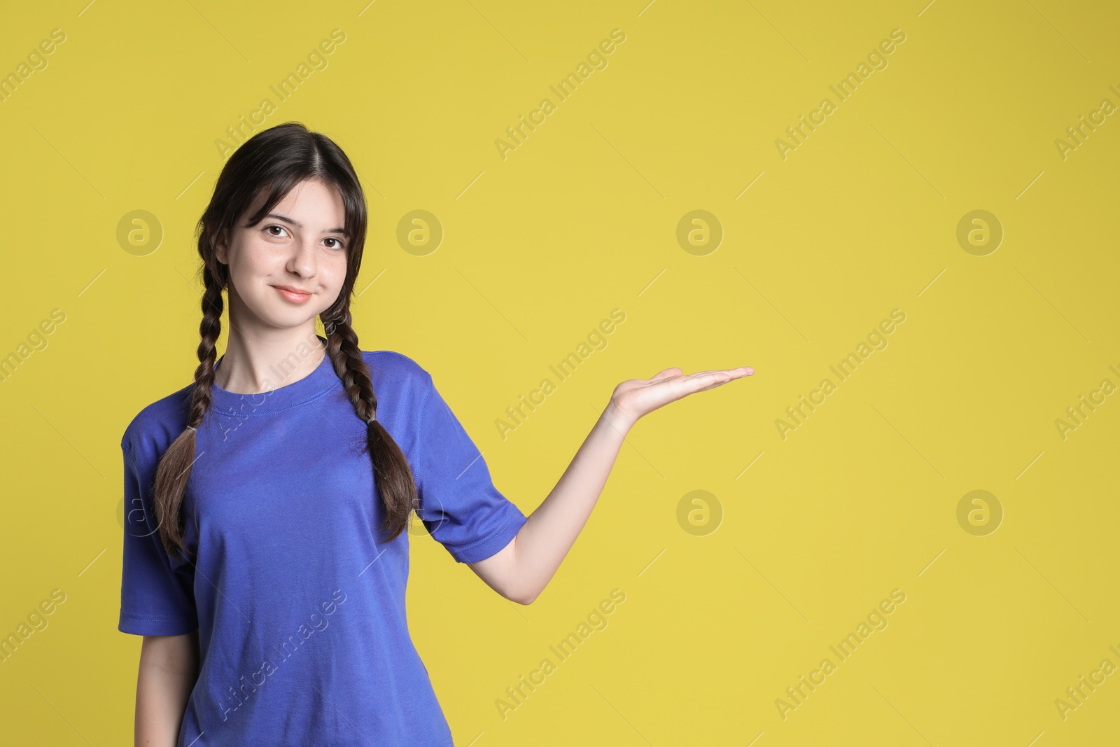 Photo of Portrait of cute teenage girl holding something on yellow background. Space for text