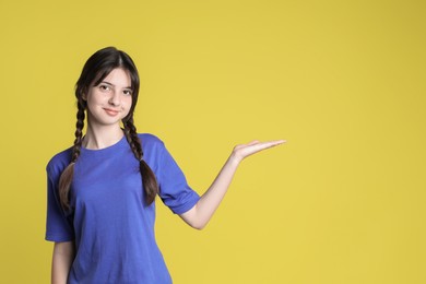 Portrait of cute teenage girl holding something on yellow background. Space for text