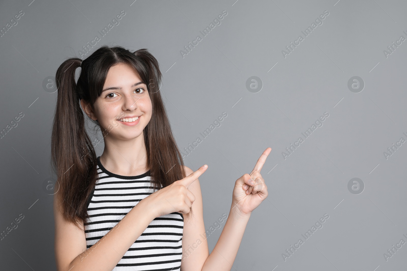 Photo of Portrait of smiling teenage girl pointing at something on grey background. Space for text