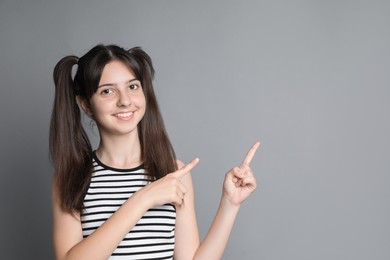 Portrait of smiling teenage girl pointing at something on grey background. Space for text