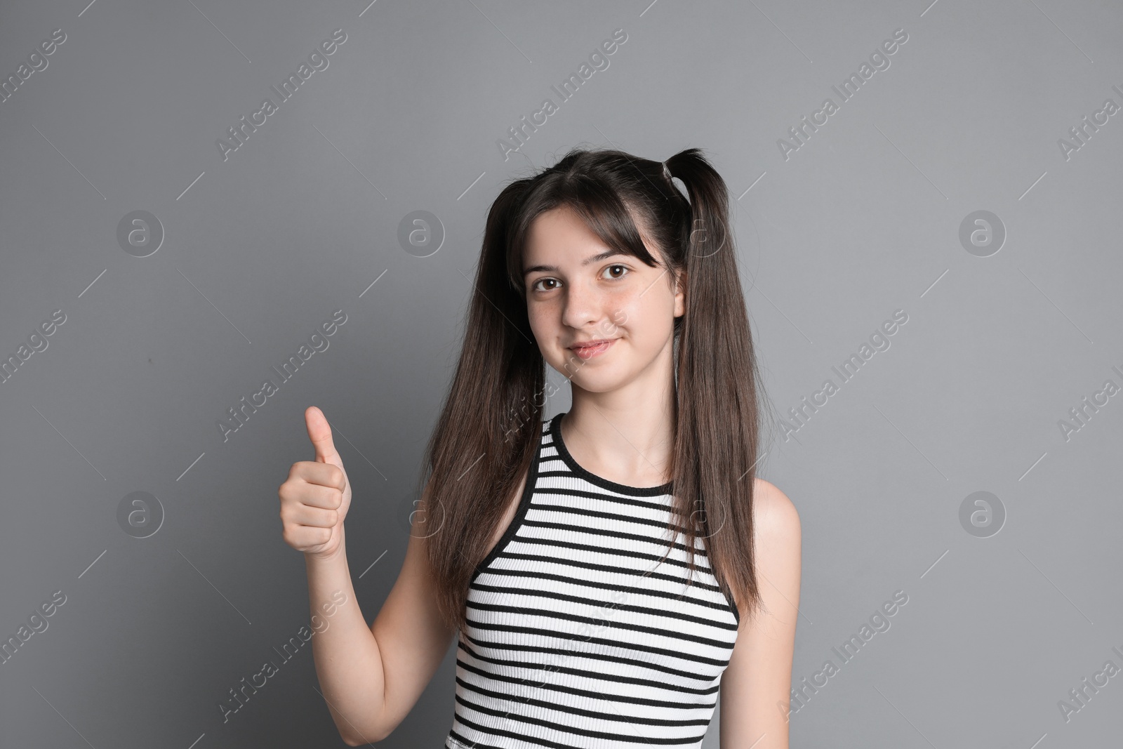 Photo of Portrait of cute teenage girl showing thumbs up on grey background