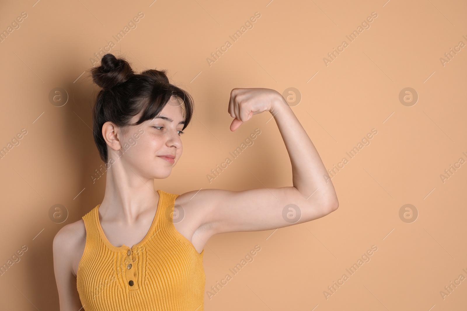 Photo of Portrait of cute teenage girl showing muscles on beige background. Space for text