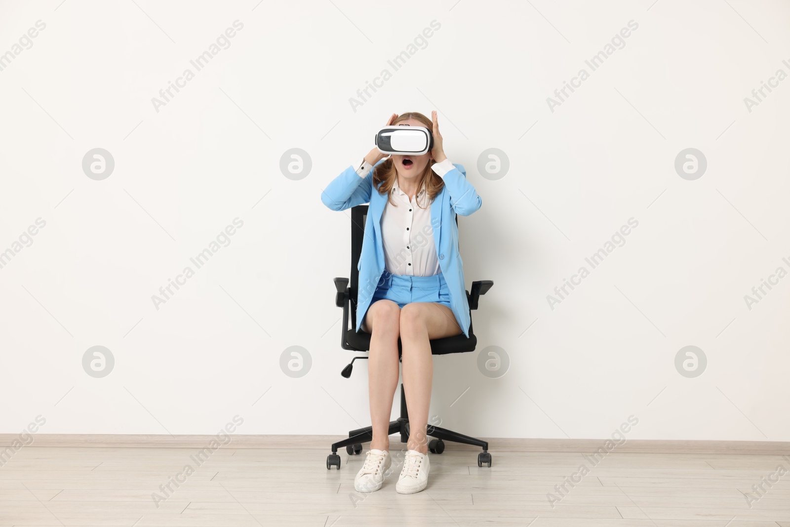 Photo of Emotional woman with virtual reality headset sitting on chair indoors