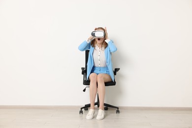 Emotional woman with virtual reality headset sitting on chair indoors