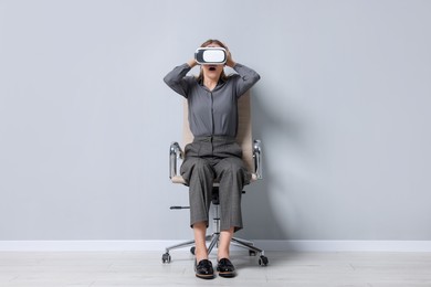 Emotional woman with virtual reality headset sitting on chair indoors