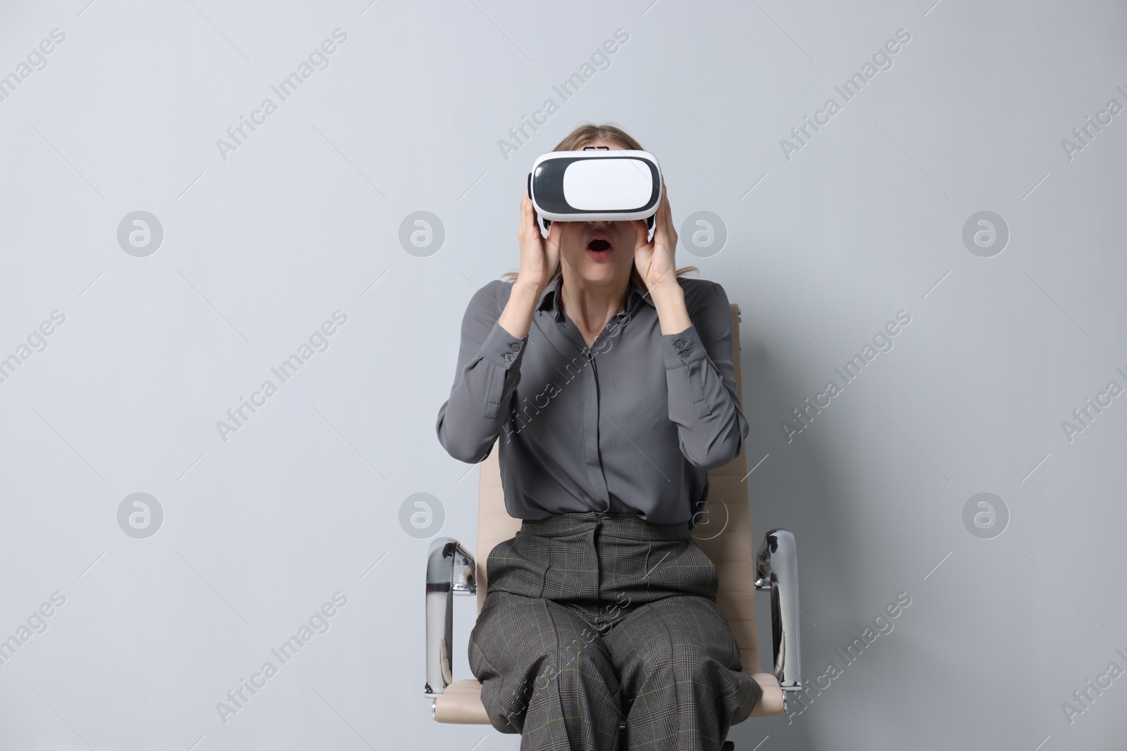 Photo of Emotional woman with virtual reality headset sitting on chair against gray background