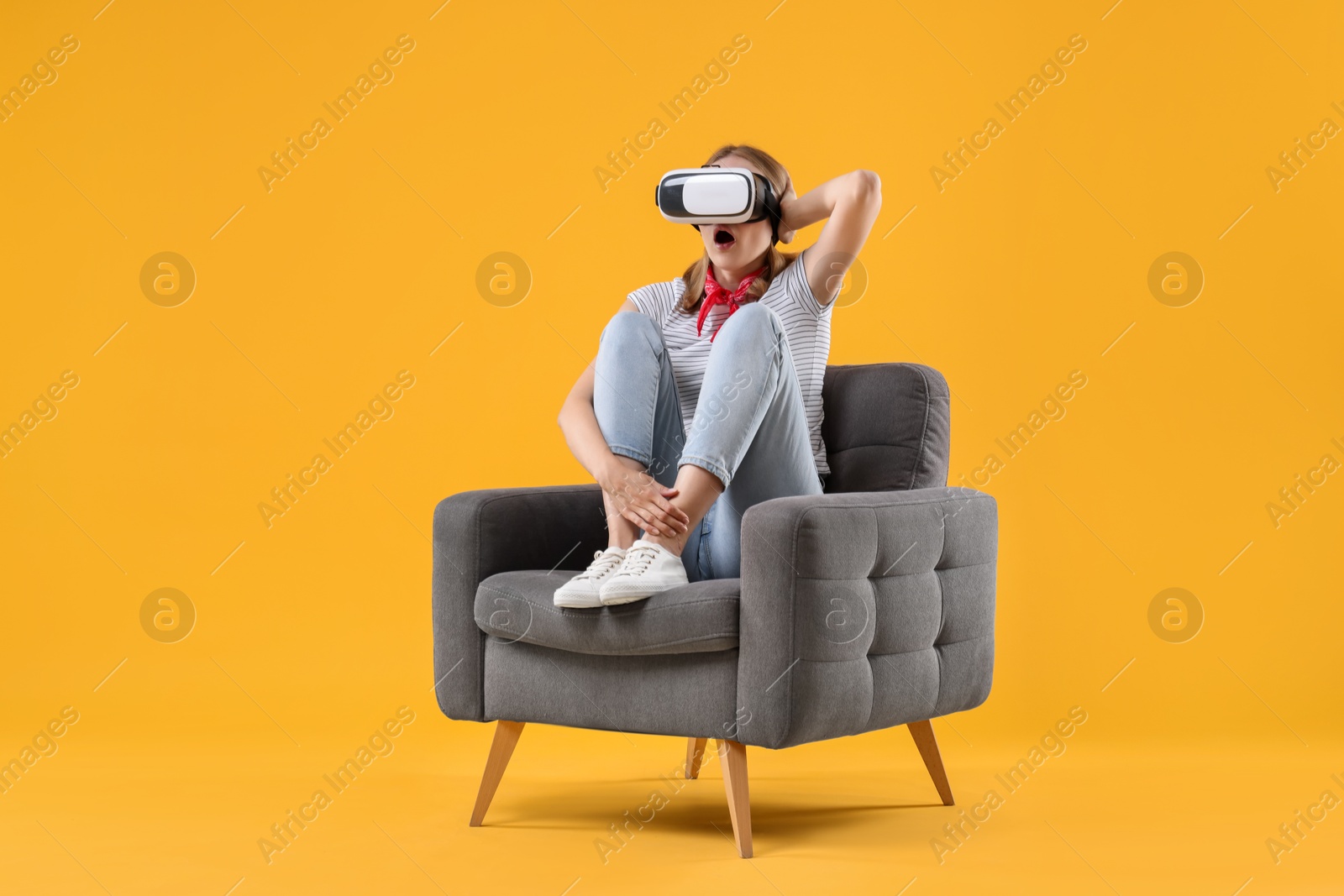 Photo of Emotional woman with virtual reality headset sitting in armchair on yellow background