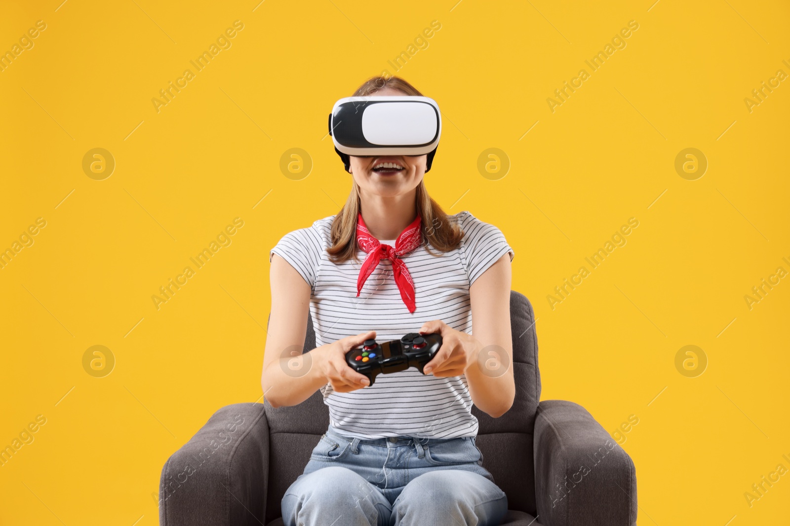 Photo of Surprised woman with virtual reality headset and controller sitting in armchair on yellow background