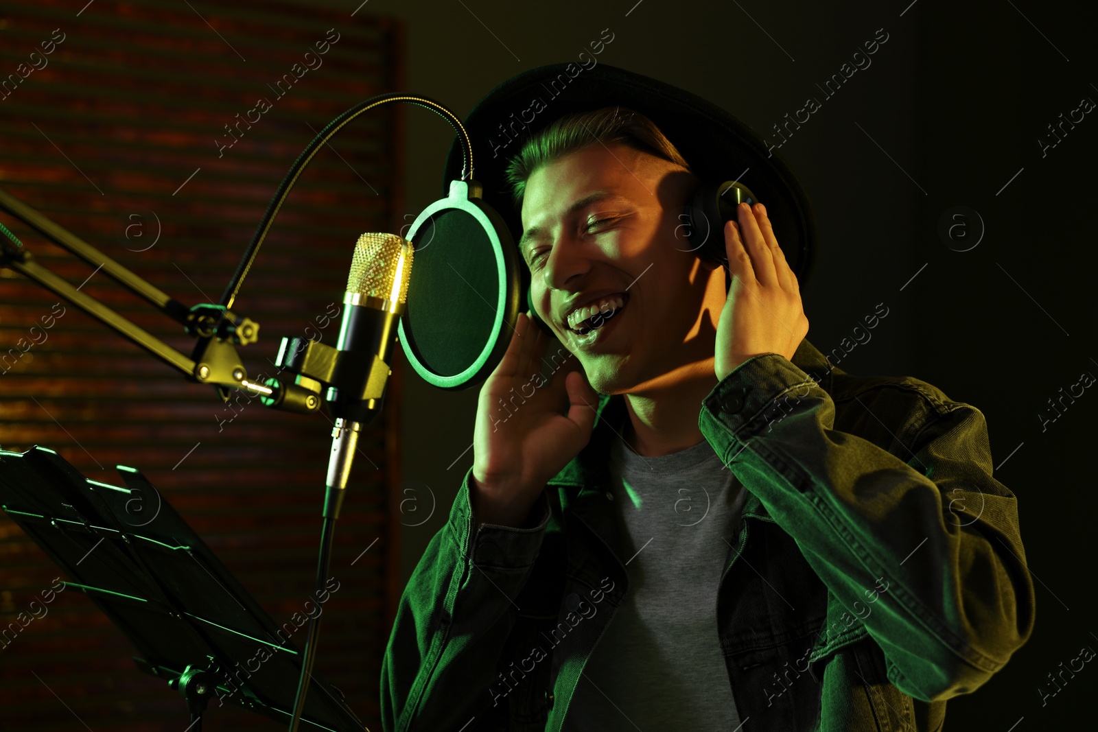 Photo of Vocalist with headphones singing into microphone in professional record studio