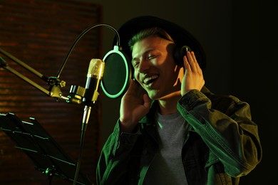 Photo of Vocalist with headphones singing into microphone in professional record studio