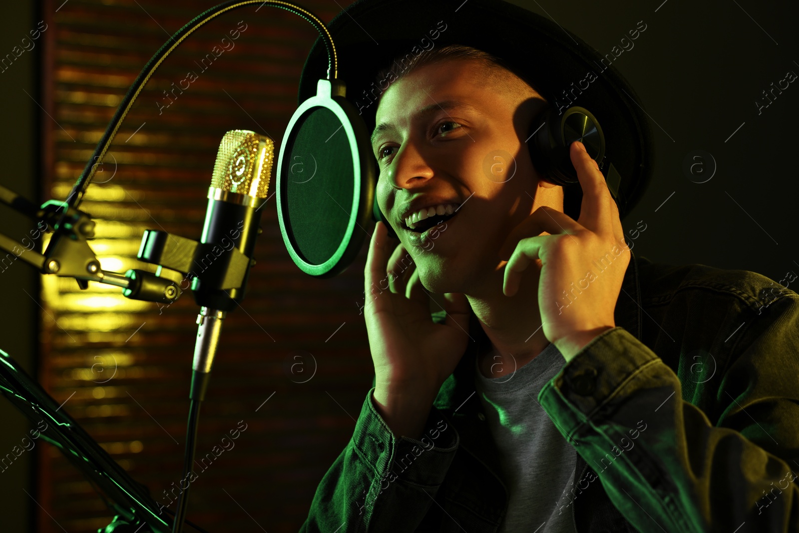 Photo of Vocalist with headphones singing into microphone in professional record studio