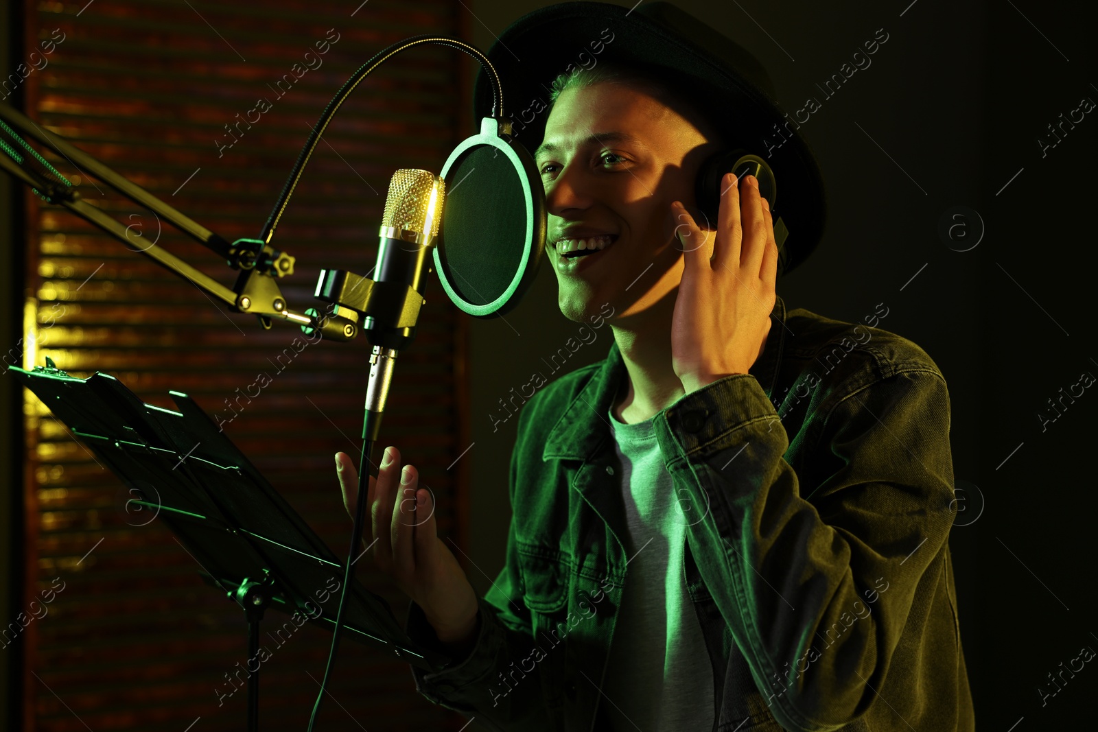 Photo of Vocalist with headphones singing into microphone in professional record studio