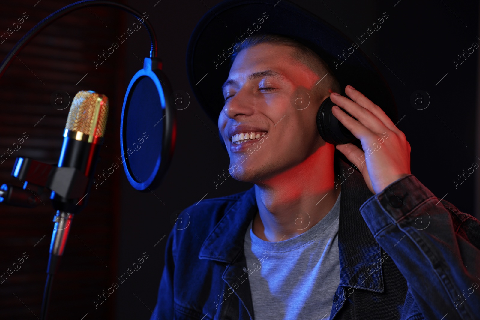 Photo of Vocalist with headphones singing into microphone in professional record studio