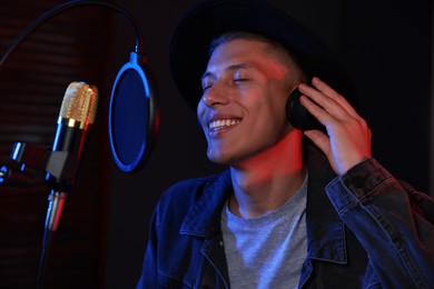 Photo of Vocalist with headphones singing into microphone in professional record studio