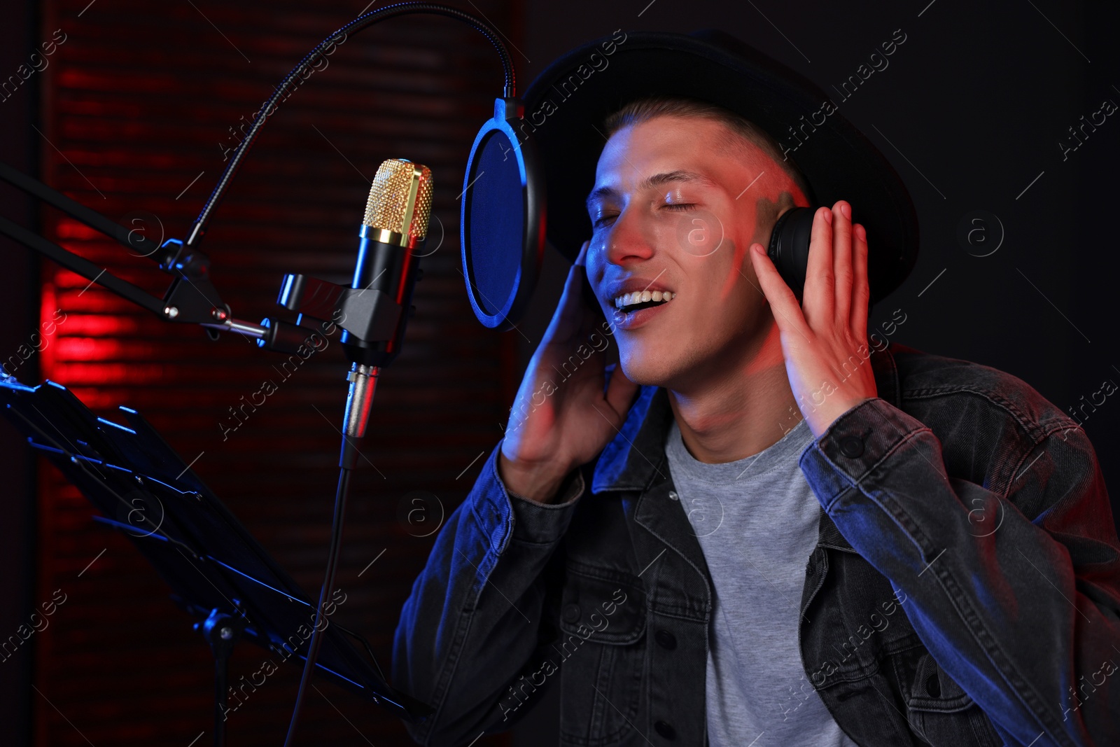 Photo of Vocalist with headphones singing into microphone in professional record studio