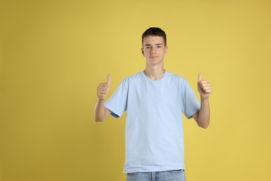 Teenage boy wearing light blue t-shirt and showing thumbs up on yellow background