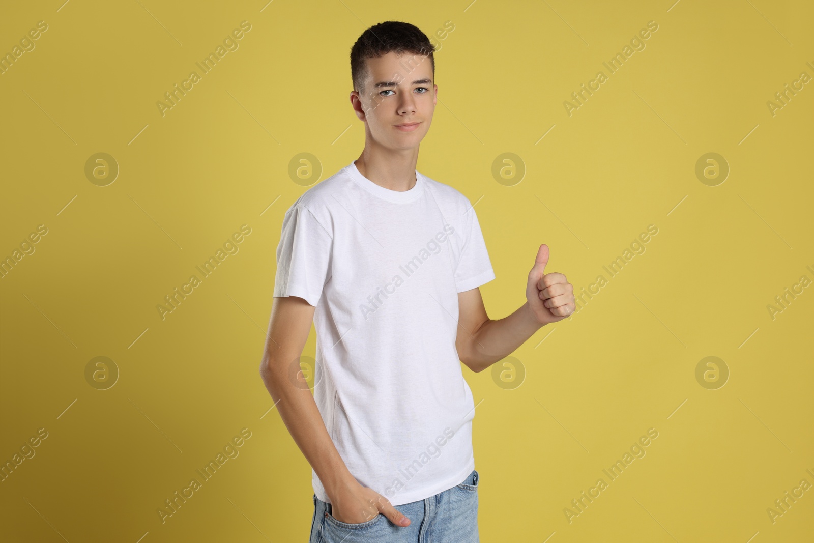 Photo of Teenage boy wearing white t-shirt and showing thumbs up on yellow background