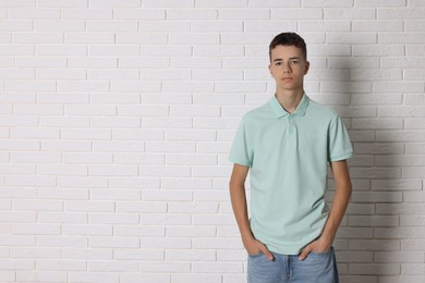 Teenage boy wearing light green t-shirt near white brick wall, space for text