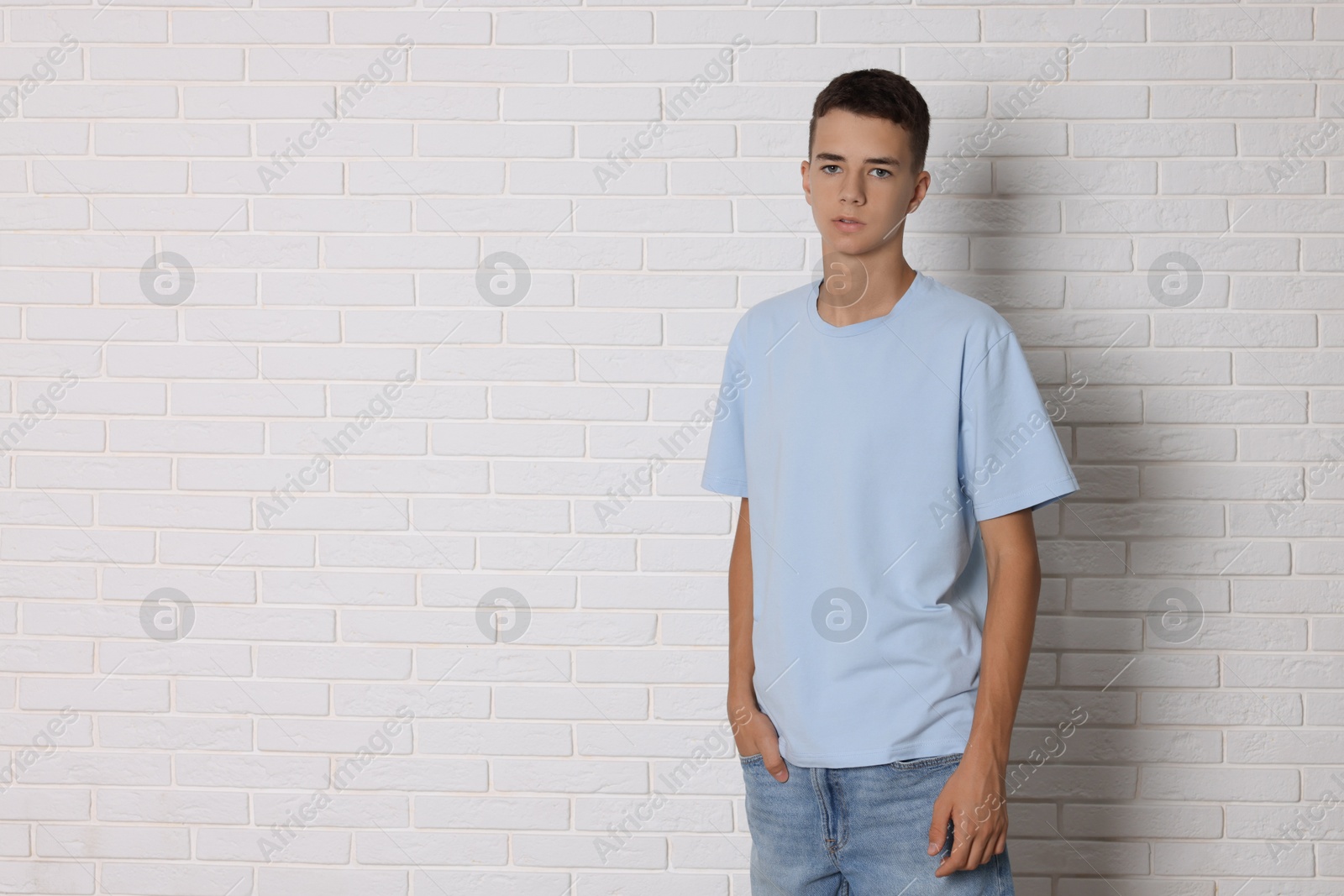 Photo of Teenage boy wearing light blue t-shirt near white brick wall, space for text