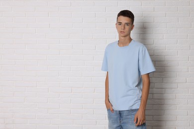 Photo of Teenage boy wearing light blue t-shirt near white brick wall, space for text