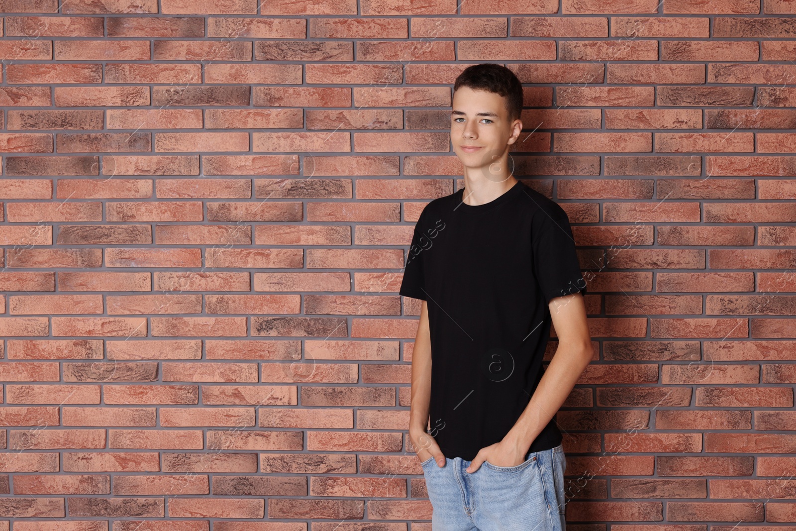 Photo of Teenage boy wearing black t-shirt near brick wall, space for text