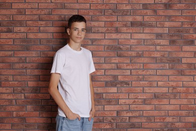 Teenage boy wearing white t-shirt near brick wall, space for text