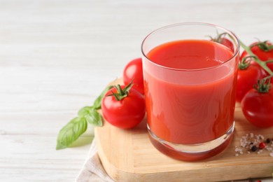 Photo of Tasty tomato juice in glass with fresh vegetables and spices on white wooden table, space for text