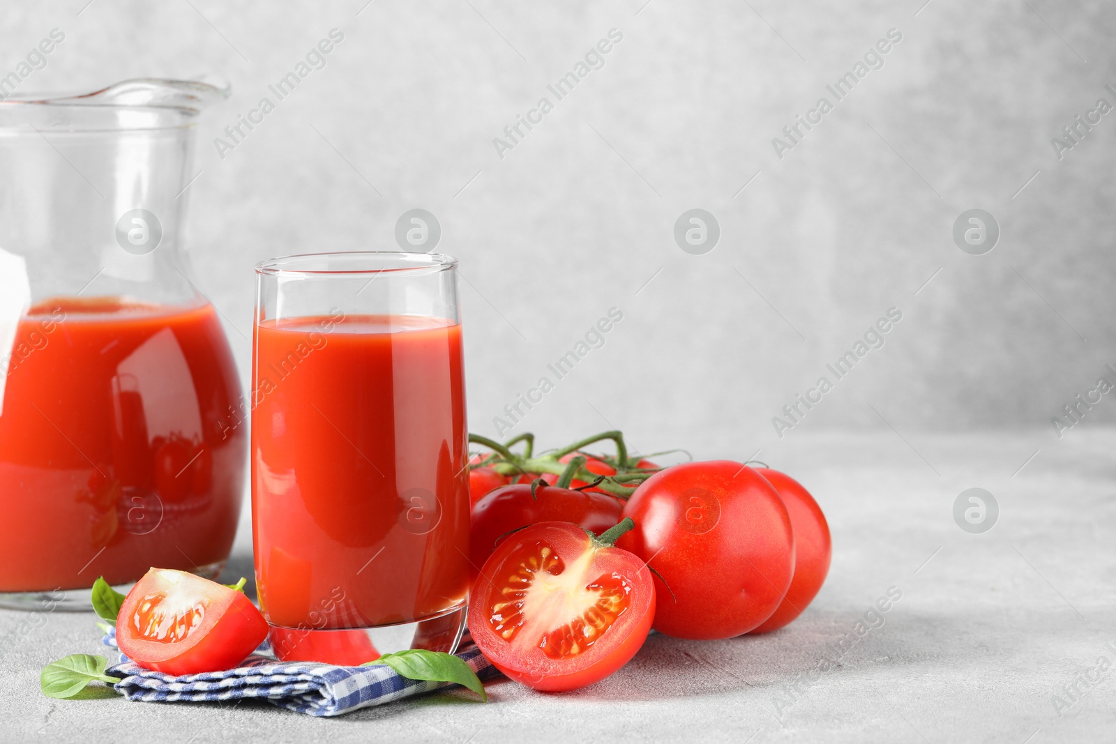 Photo of Tasty tomato juice with fresh vegetables and basil leaves on light grey table, space for text