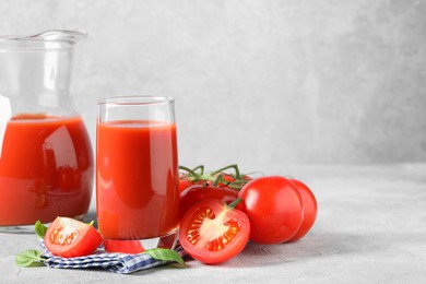 Tasty tomato juice with fresh vegetables and basil leaves on light grey table, space for text